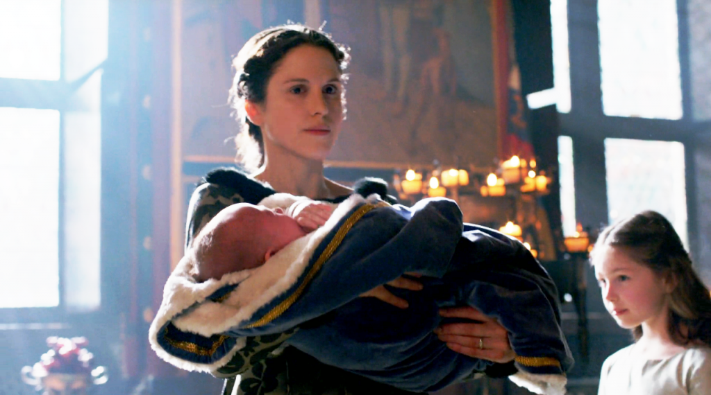 Still de Margaret Beaufort (Amanda Hale) segurando o pequeno  Príncipe Richard no colo 